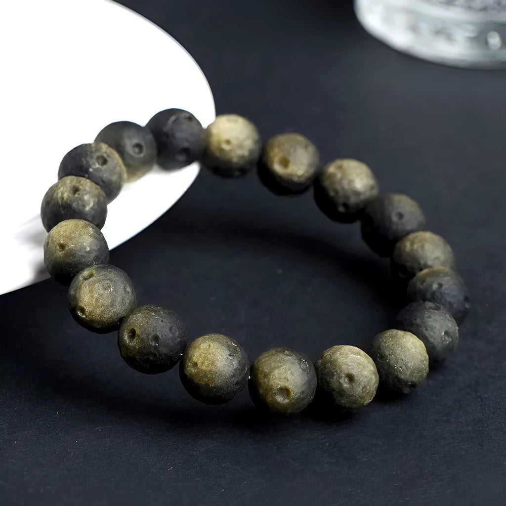 Natural obsidian crater ball bracelet with a ground texture in silver stone or gold colours on a wrist.