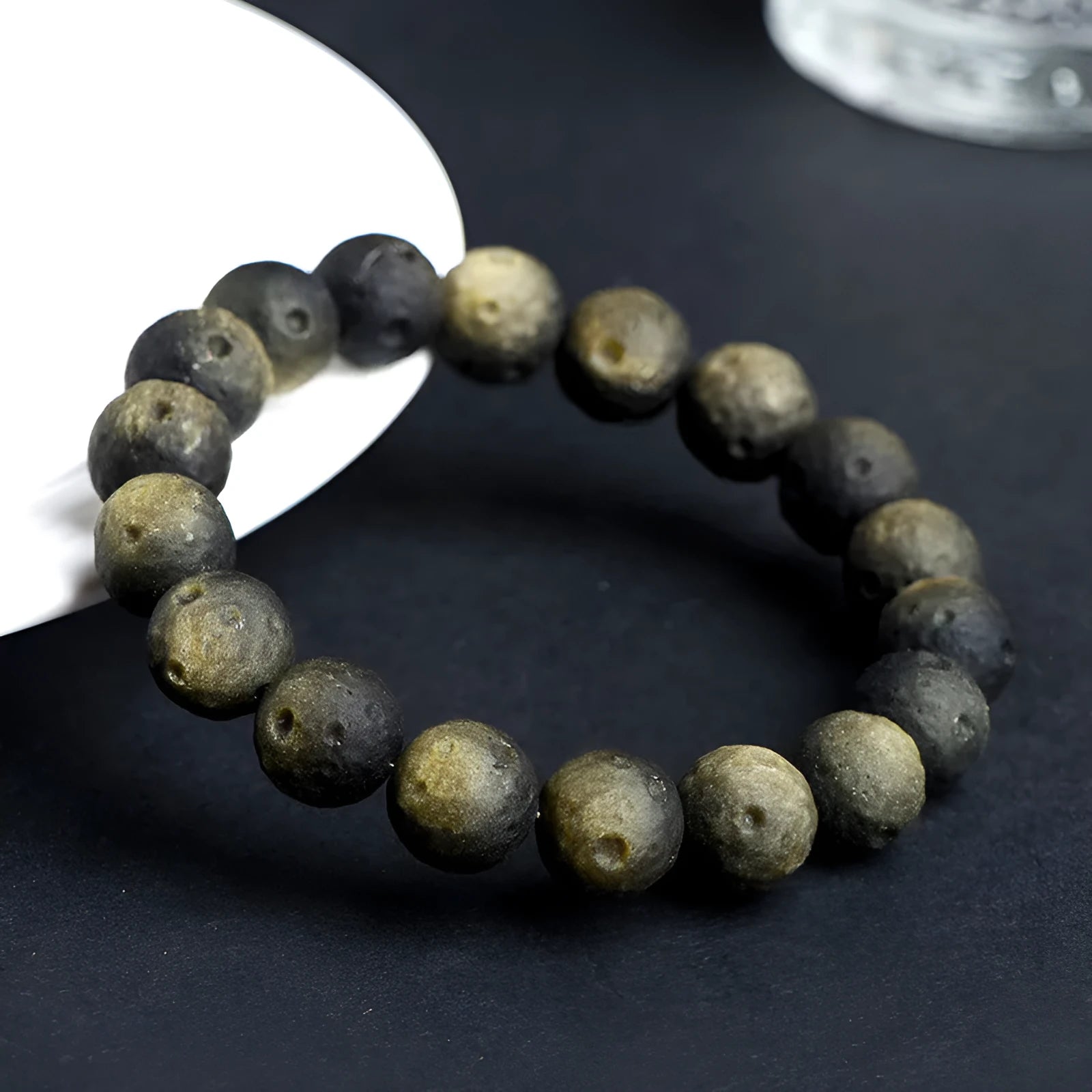 Natural obsidian crater ball bracelet with a ground texture in silver stone or gold colours on a wrist.