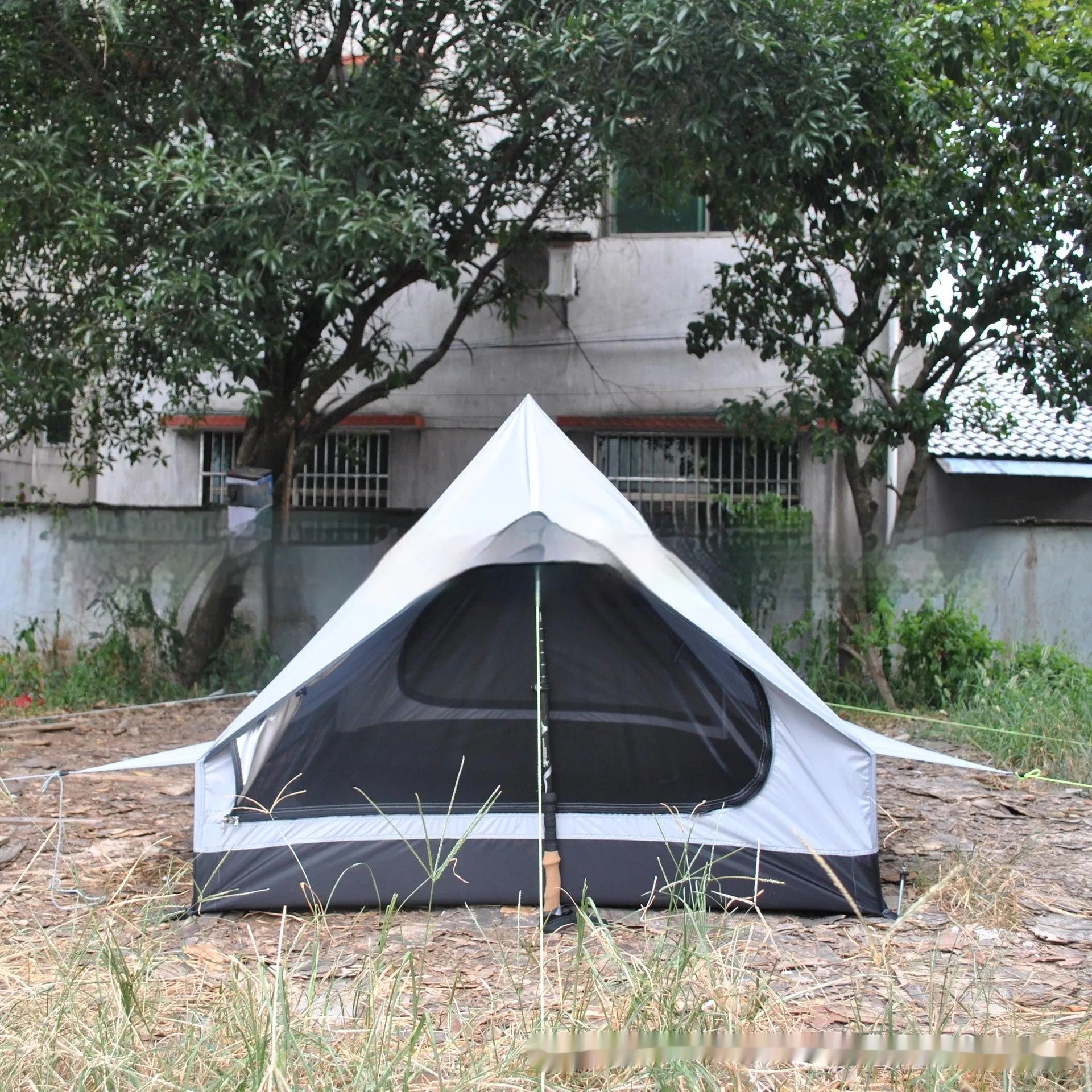 Lightweight brown A-line hiking tent set up with hiking cane supports in outdoor setting