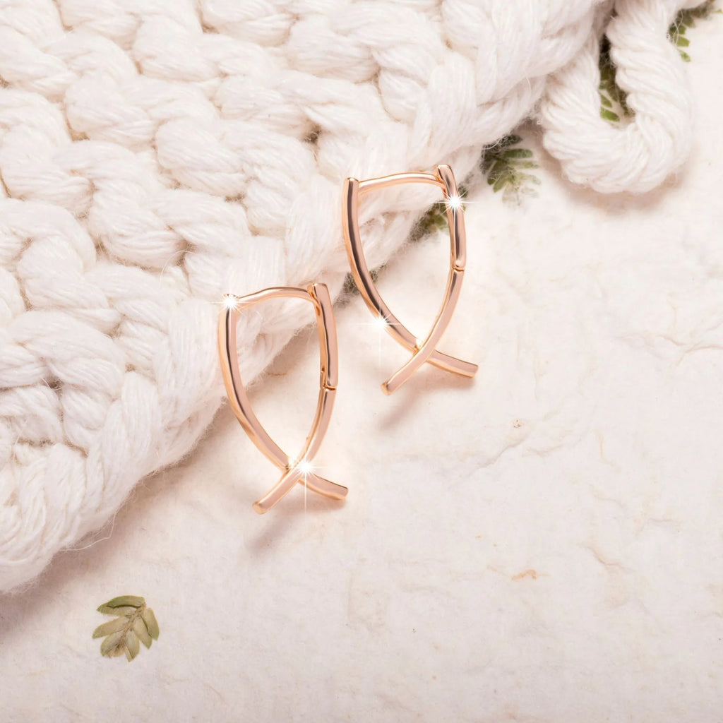 A pair of rose gold cross shaped drop earrings on a plain background.