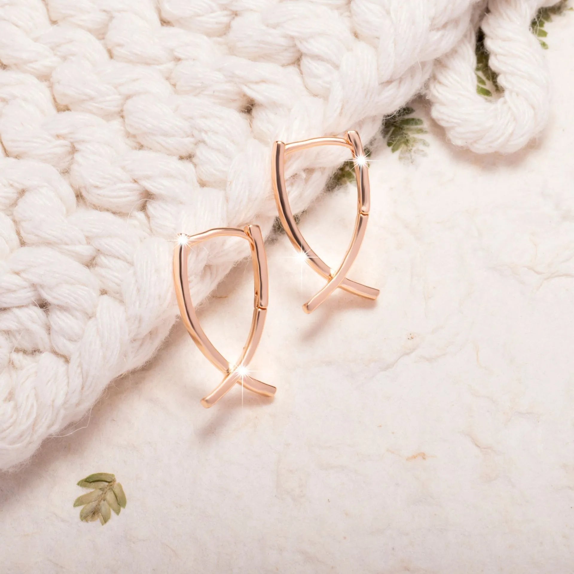 A pair of rose gold cross shaped drop earrings on a plain background.