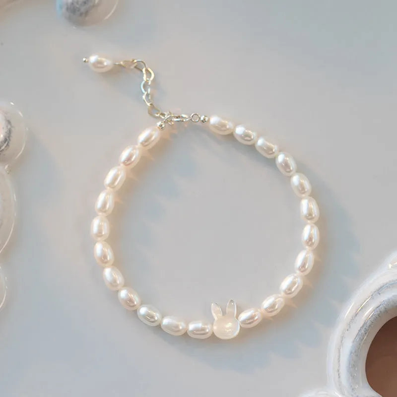White pearl and 925 silver rabbit charm bracelet on a model's wrist, showing adjustable elastic string.