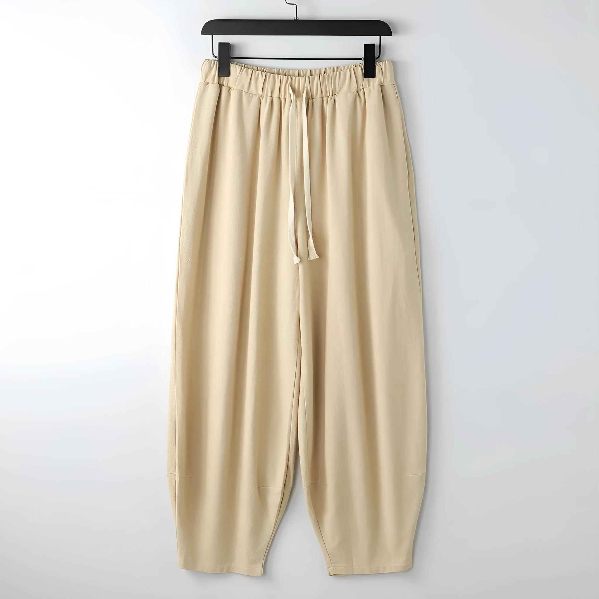 Man wearing loose grey linen harem pants with tied ankles, showing tapered leg fit.