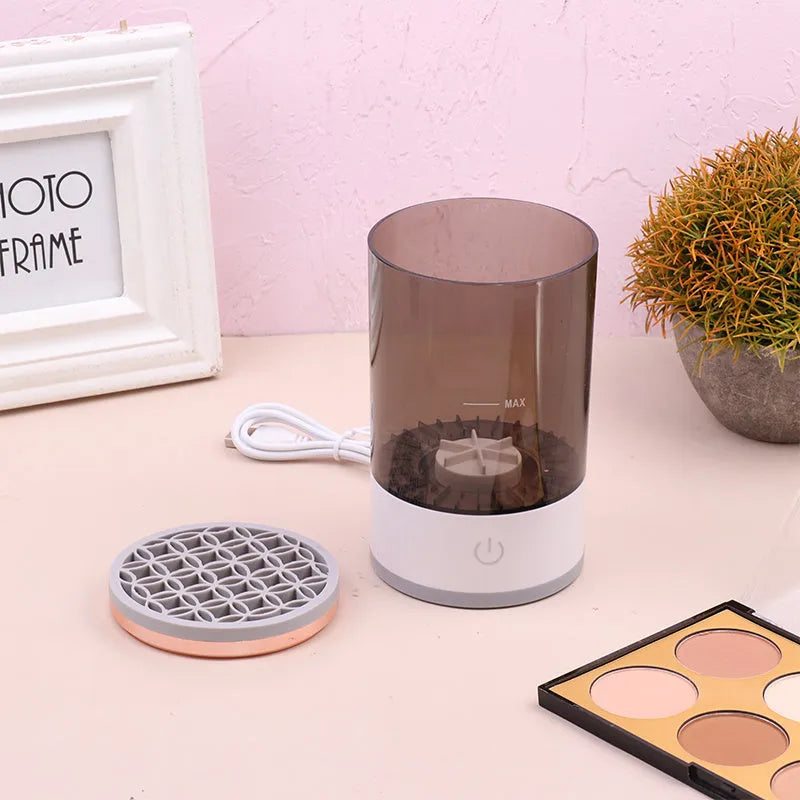Grey and white electric makeup brush cleaner with USB charging cable on a wooden surface