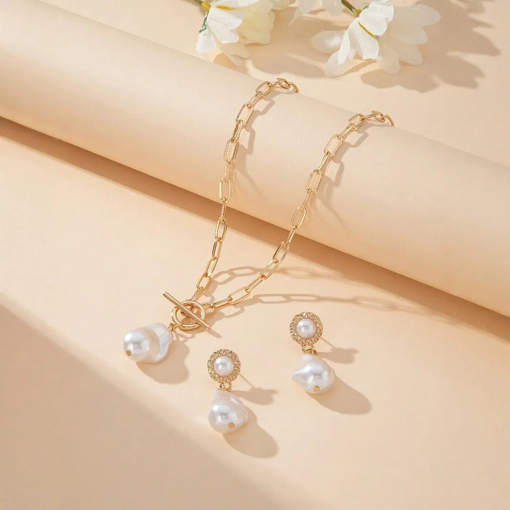 Gold tone retro style necklace and matching pearl ear studs set for women on a flat surface.