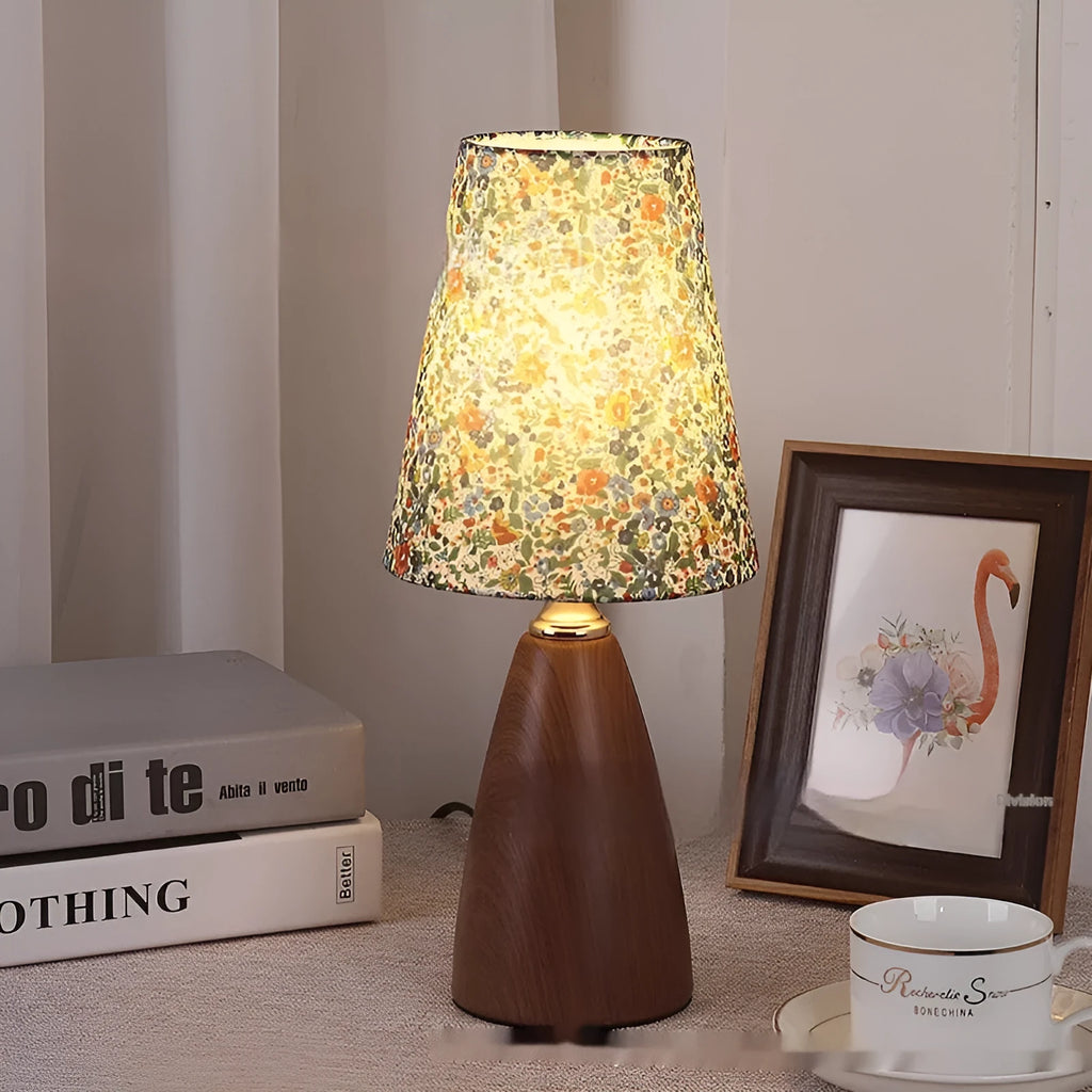 Tapered floral ceramic table lamp with remote control on a wooden surface.