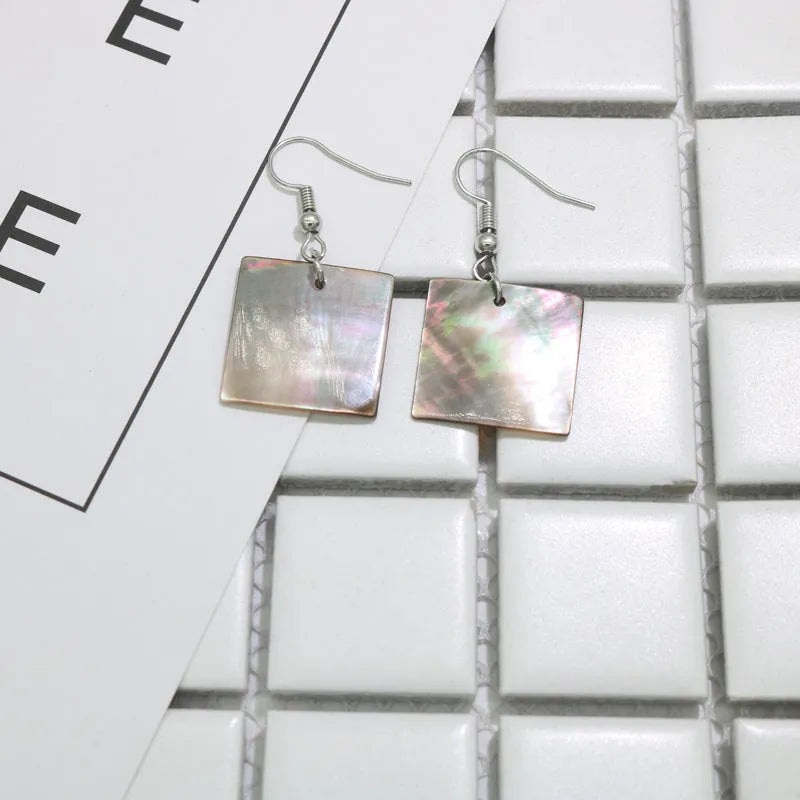 A pair of geometric shell earrings in a square panther design next to a rectangular shell design on a neutral background.