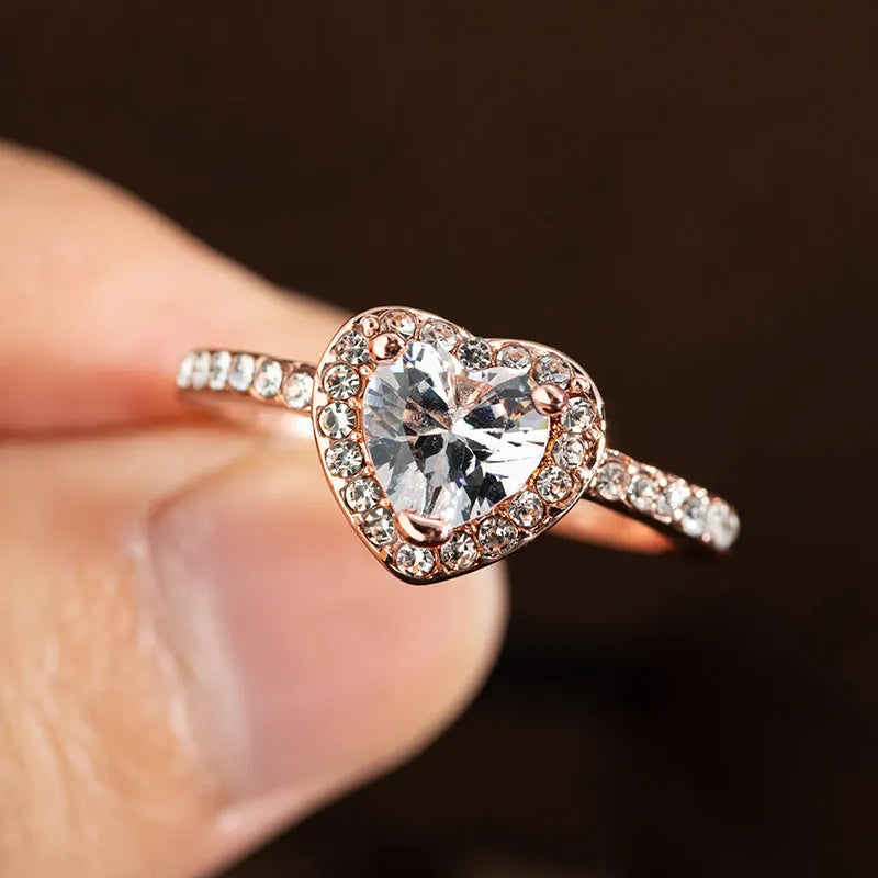 Women's heart-shaped wedding ring with central crystal on white copper band in rose gold finish.