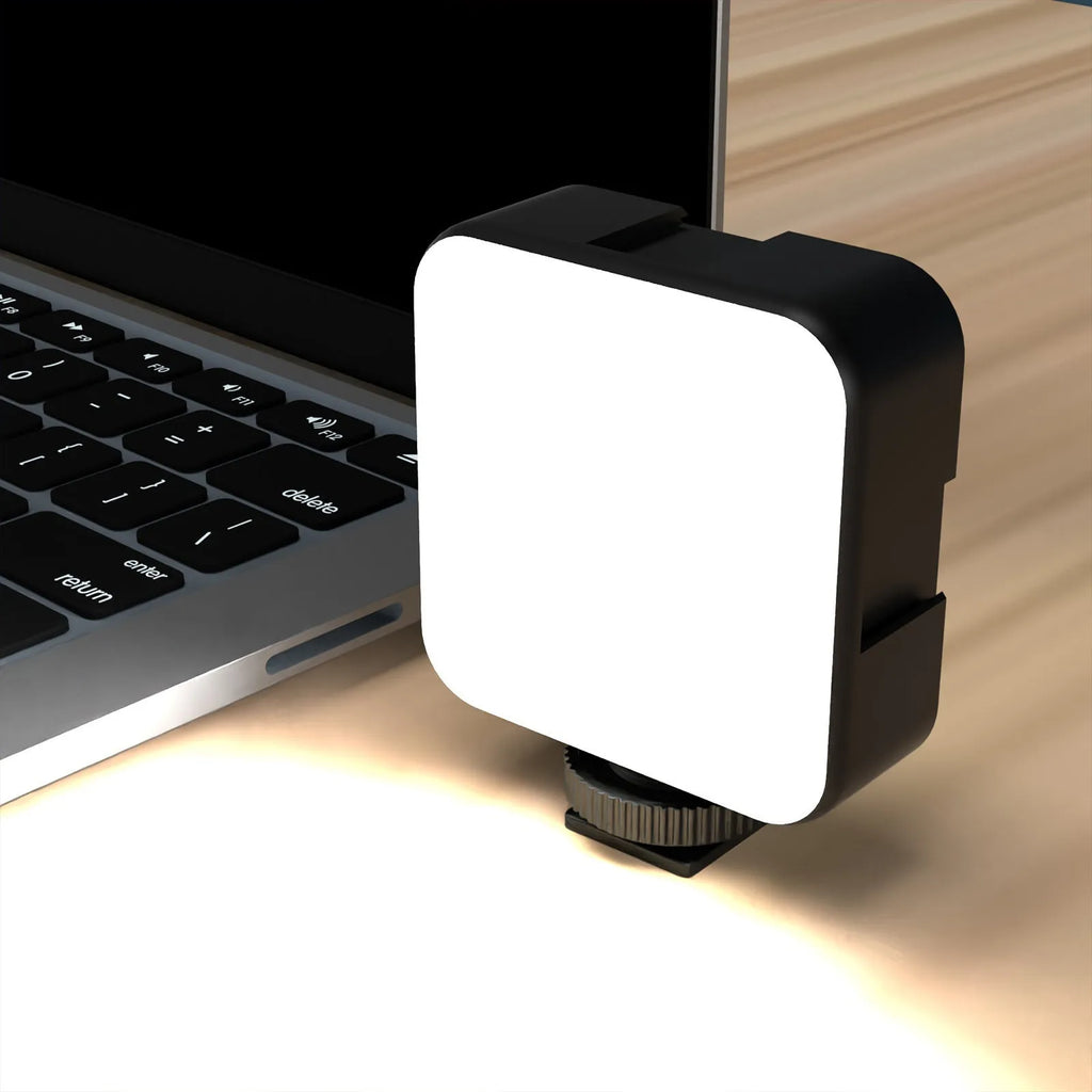 Silver 5600K LED video light cube clipped onto a laptop, with shelf and wire included