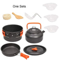 Orange folding camping cookware set with pots, pan, spoons, bowls in mesh bag on outdoor table
