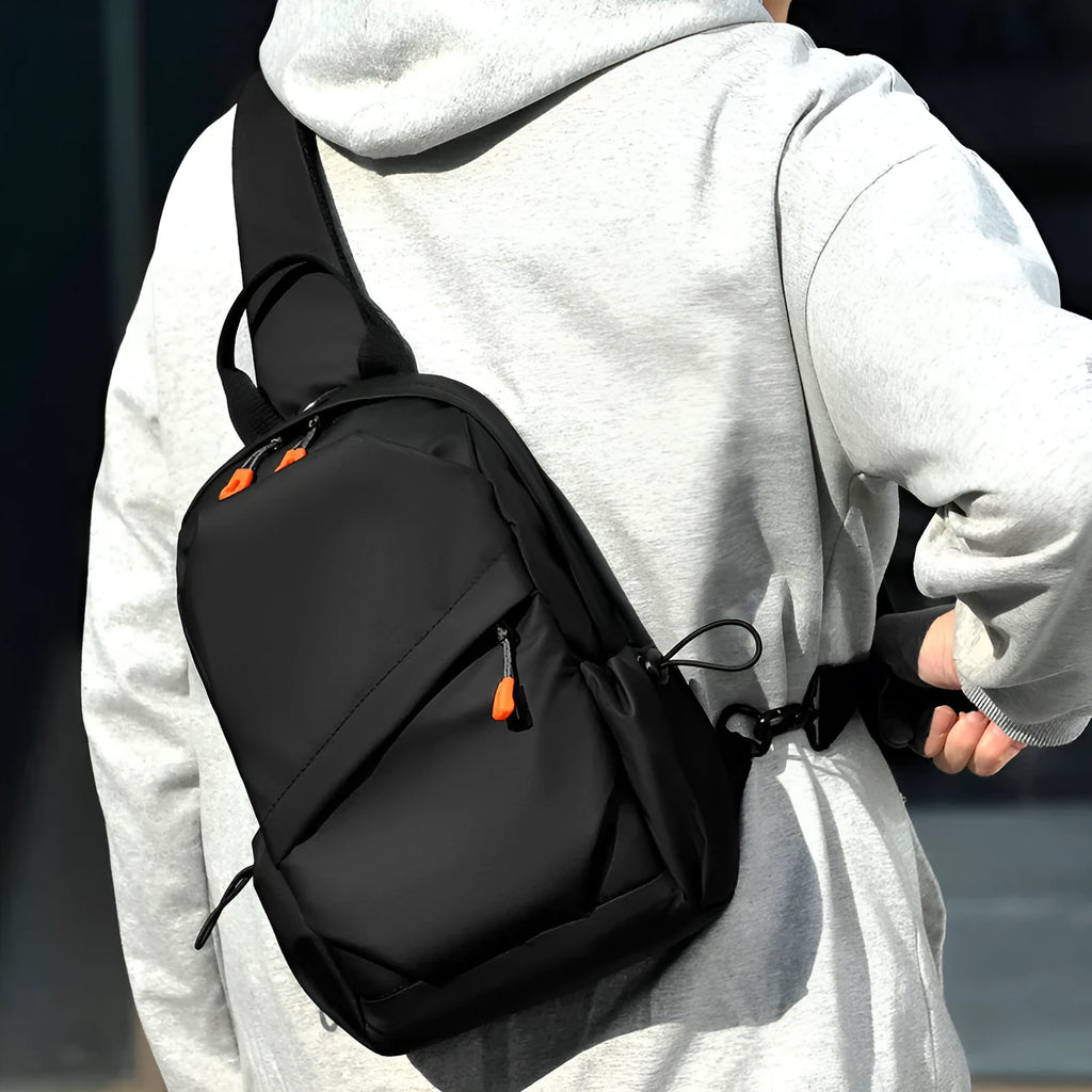Men's black polyester crossbody bag with a single shoulder strap, shown in a casual setting.