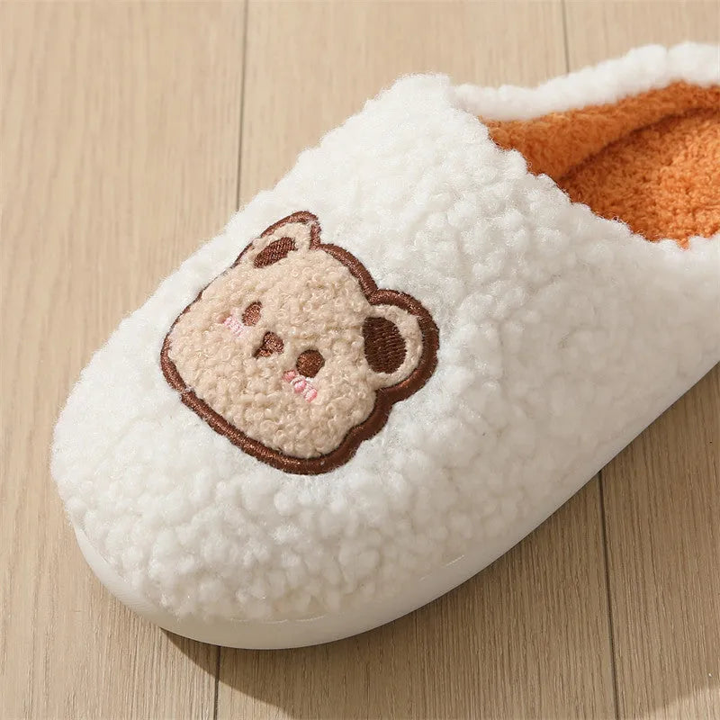 Pair of cute cartoon bear winter slippers with plush upper and non-slip TPR sole on a bedroom floor