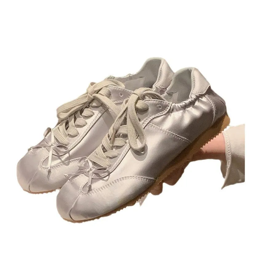 Women's silver grey satin ballet flats with round toe and white lace-up front on a plain background.