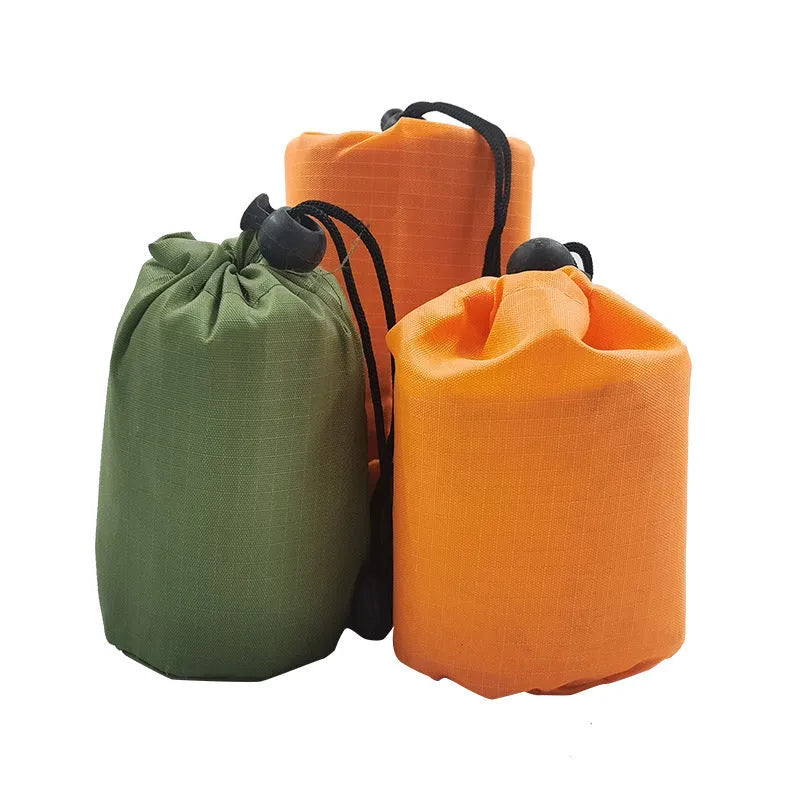 Orange emergency survival blanket unfolded showing reflective inner surface, with folded sleeping bag and tent beside it in nylon bag