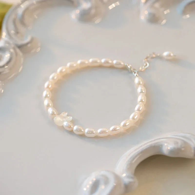White pearl and 925 silver rabbit charm bracelet on a model's wrist, showing adjustable elastic string.