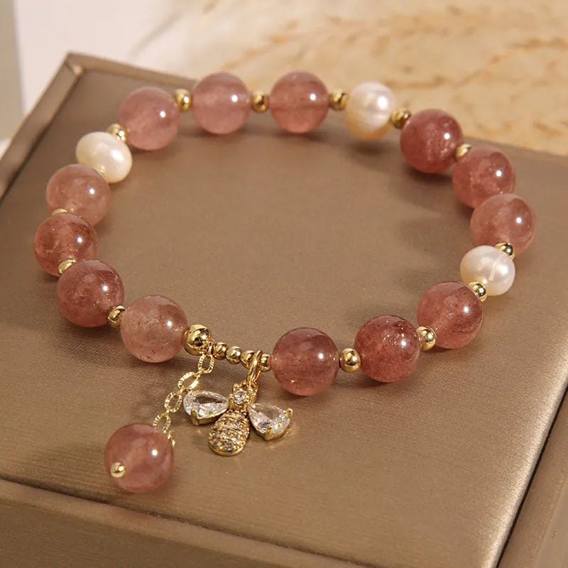 Close-up of a women's bracelet with pink strawberry quartz beads, white freshwater pearls, and sparkling zircon charms on an alloy chain.