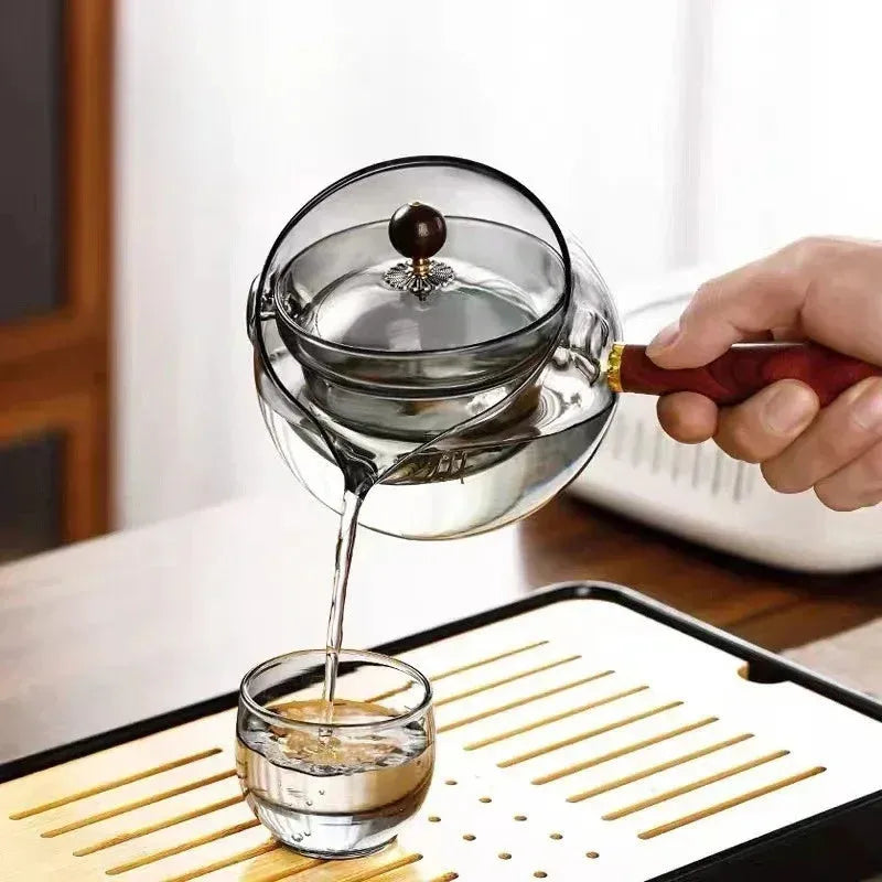 Transparent rotary glass teapot with wooden handle and built-in infuser on countertop