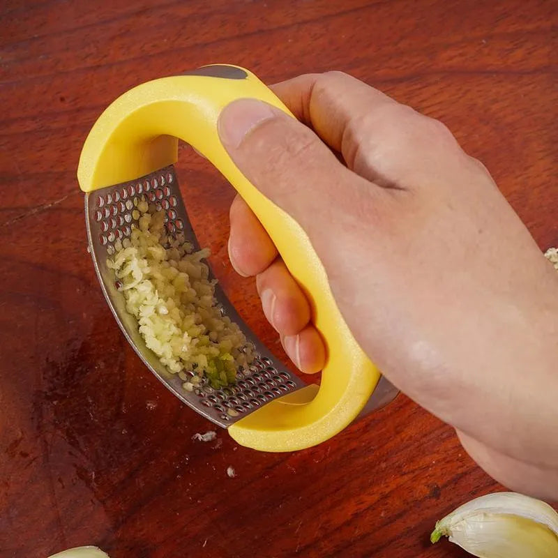 Stainless steel garlic press with curved ergonomic design and non-slip handle in assorted colours.