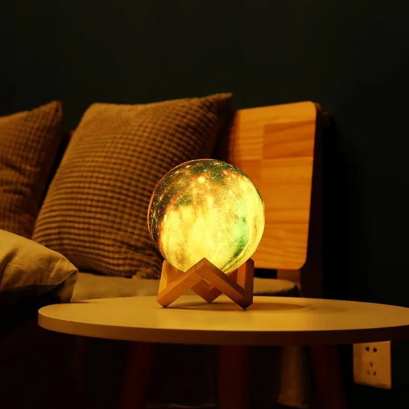3D printed white lunar sphere night light glowing with soft yellow light on a dark surface.