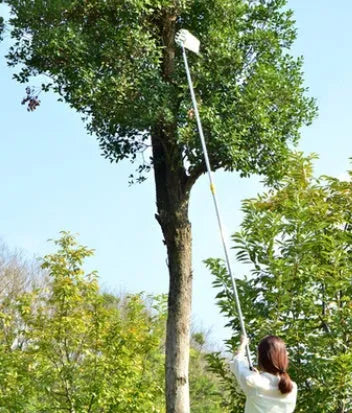 Silver metal fruit picker with serrated ring and cotton bag resting against an orchard tree