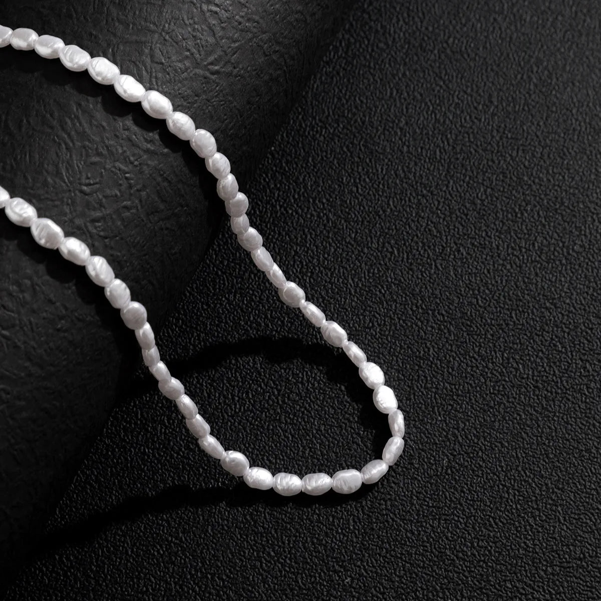 Men's white U-shaped pearl necklace with mother-of-pearl pendant on a pearl chain.