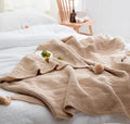 Nordic-style fringed knit acrylic blanket in a neutral colour, shown on a sofa.