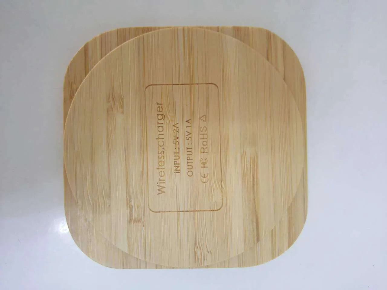 Square natural bamboo 5W QI wireless charging pad on a wooden surface.