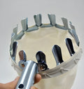 Silver metal fruit picker with serrated ring and cotton bag resting against an orchard tree