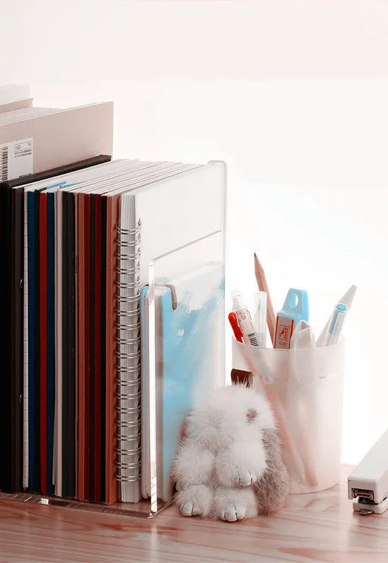 Transparent acrylic bookshelf holding a small stack of books on a wooden desk.