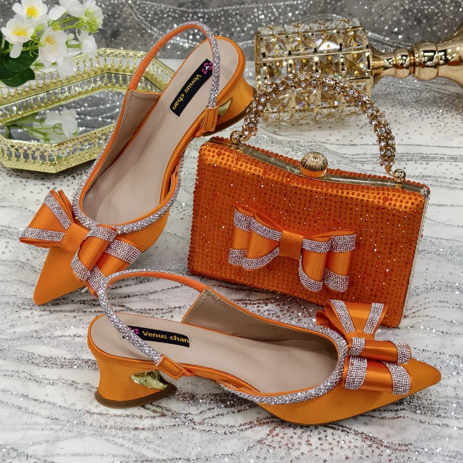 Women's black pointed toe sandals with elastic band and matching square rhinestone clutch bag on a neutral background.