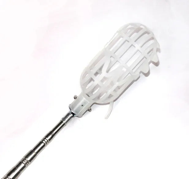Silver metal fruit picker with serrated ring and cotton bag resting against an orchard tree