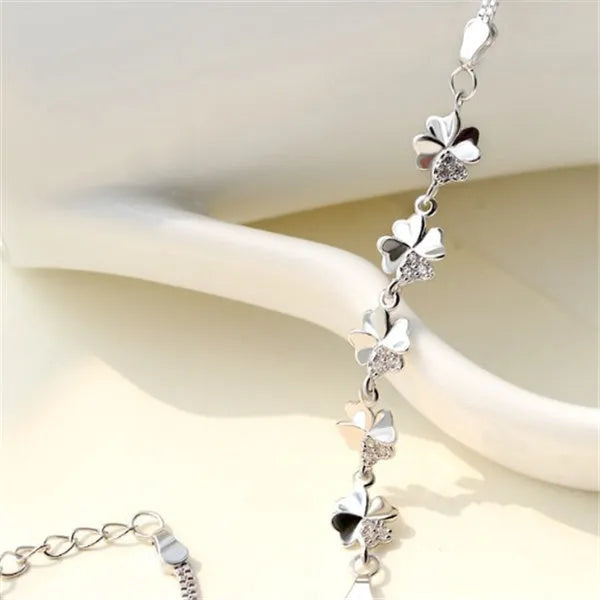 Silver four-leaf clover bracelet with leaf pendant on a plain background