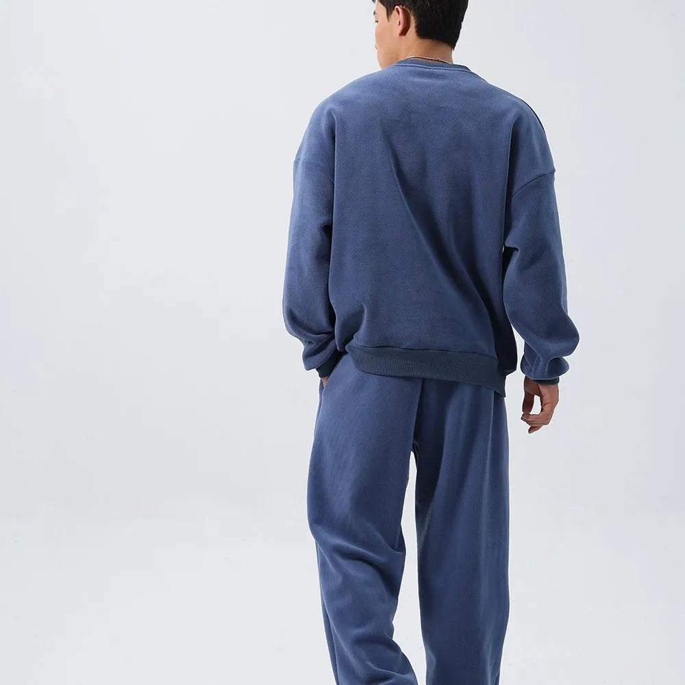 Men's black polar fleece sports suit with crew neck jacket and loose fit trousers laid flat.