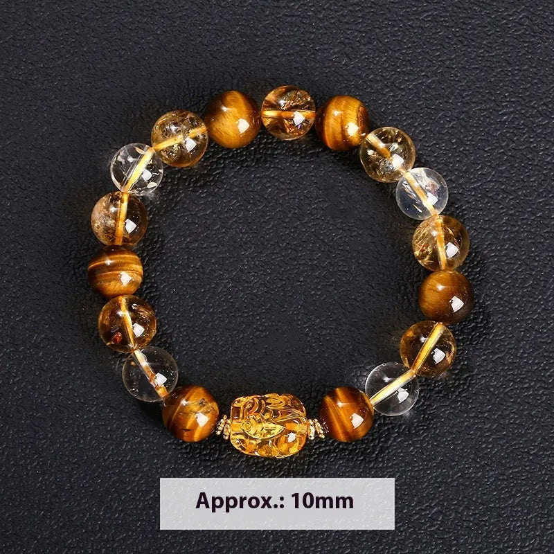 A close-up of a beaded bracelet with yellow banded Tiger's Eye and translucent citrine 10mm beads and a metallic Pi Xiu charm.