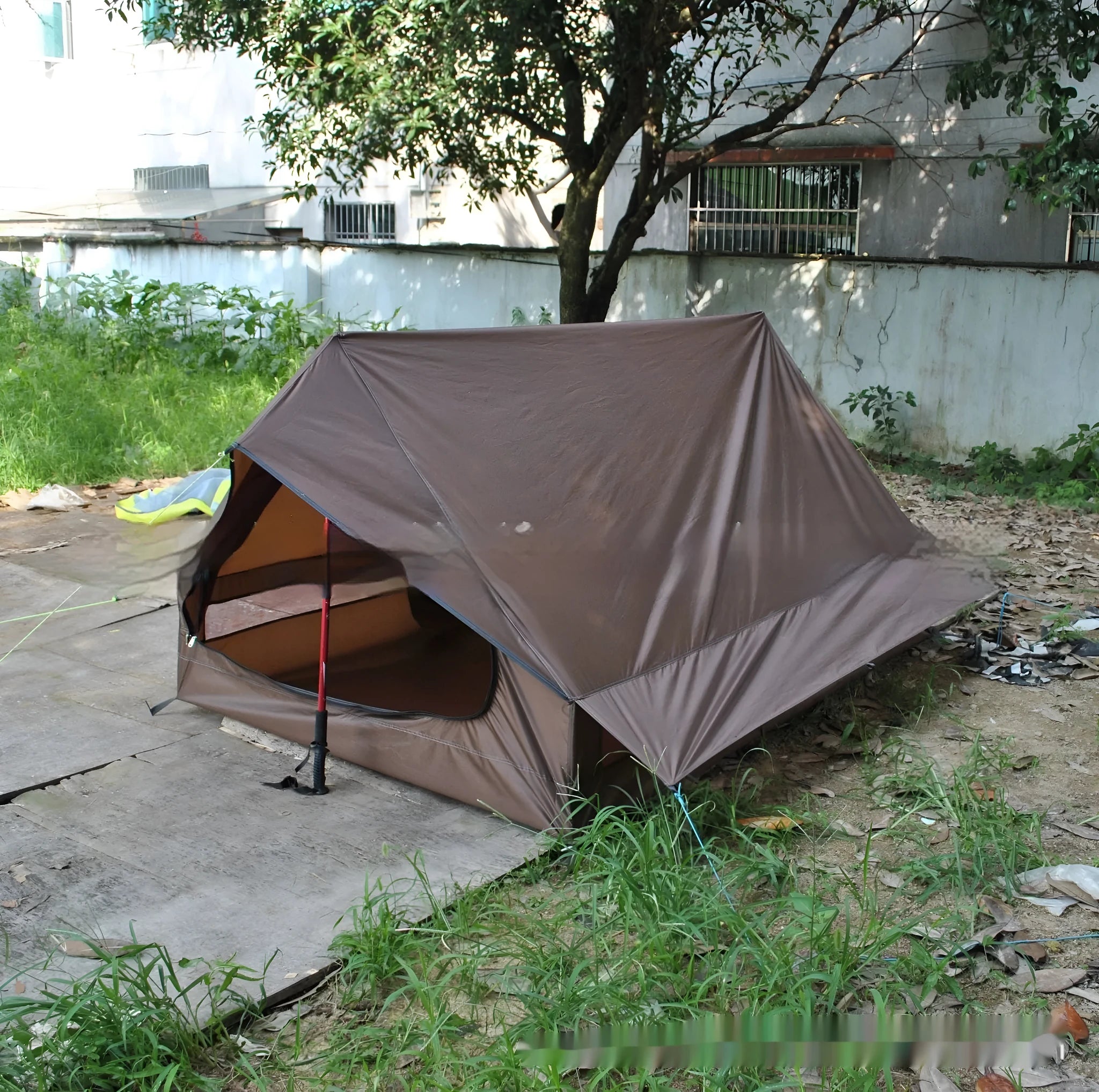 Lightweight brown A-line hiking tent set up with hiking cane supports in outdoor setting