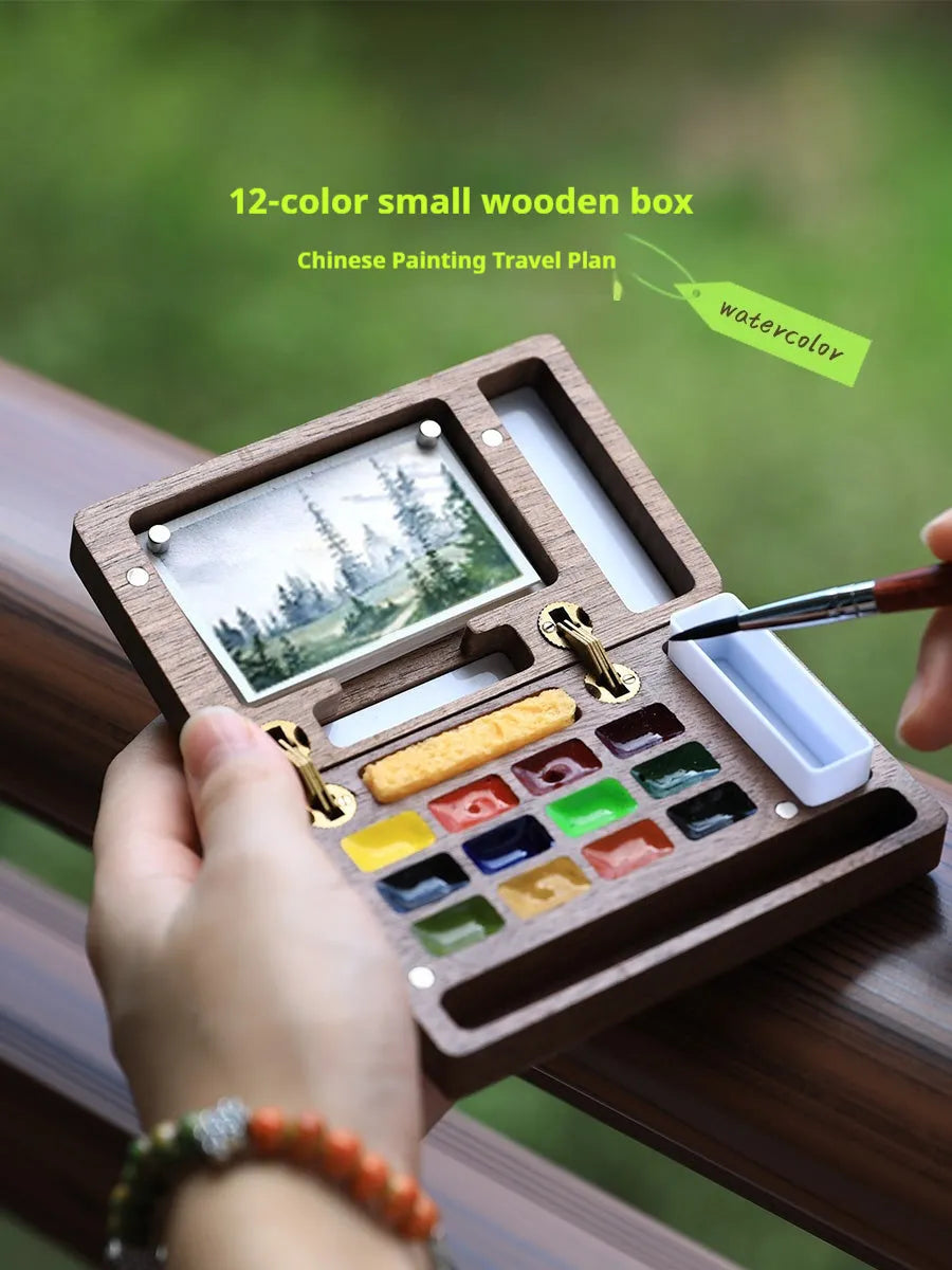 Mini walnut-finish wooden watercolour paint box open to show internal compartments with pigment pans.