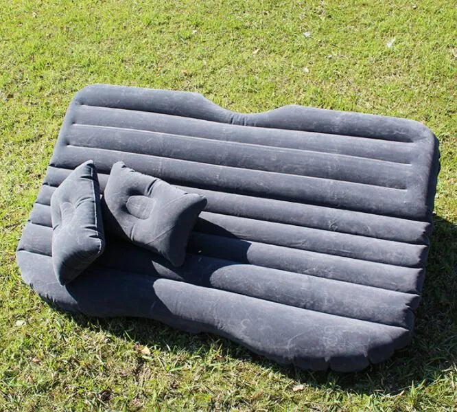 Black inflatable car bed with flocked material set up in the back of a five-seater vehicle, showing two pillows.
