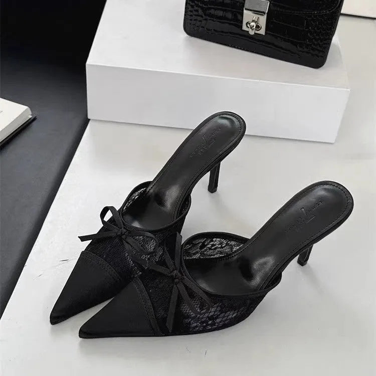 Women's light brown lace high heels with a pointed toe and a black bowknot detail on the front.