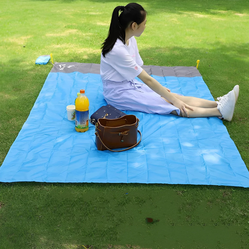 Blue and grey waterproof camping mat with TPU coating spread on grass, with storage sack and pegs nearby