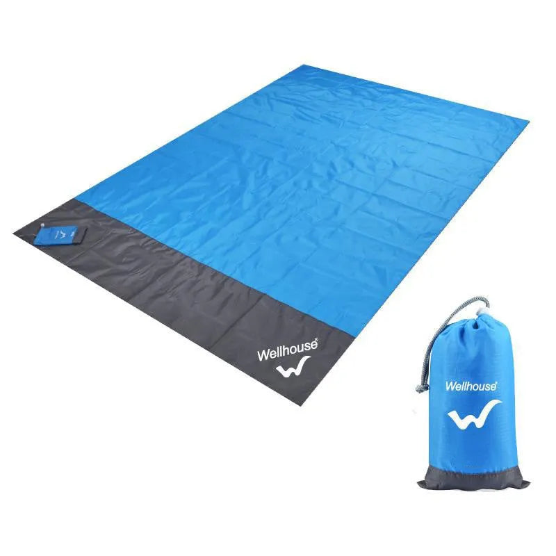 Blue and grey waterproof camping mat with TPU coating spread on grass, with storage sack and pegs nearby