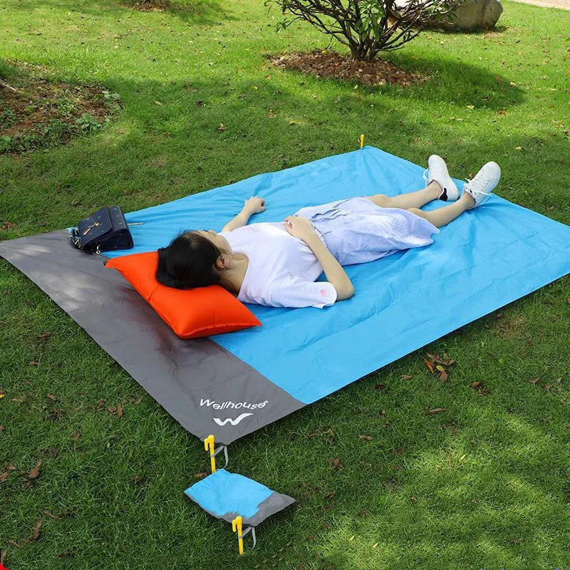 Blue and grey waterproof camping mat with TPU coating spread on grass, with storage sack and pegs nearby