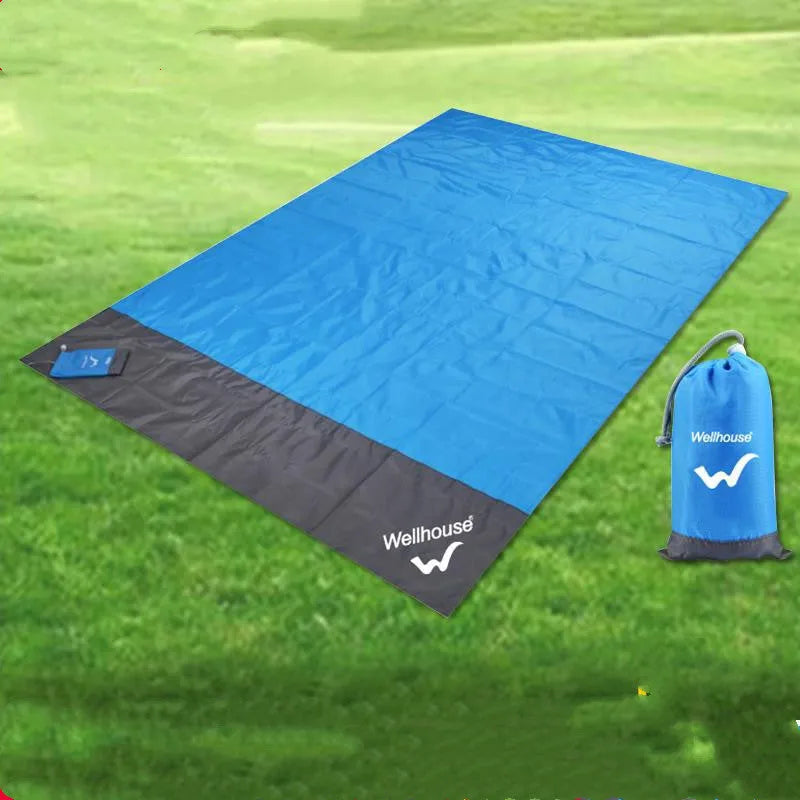 Blue and grey waterproof camping mat with TPU coating spread on grass, with storage sack and pegs nearby