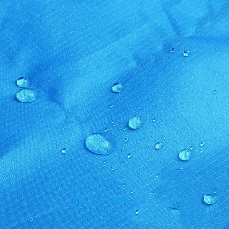 Blue and grey waterproof camping mat with TPU coating spread on grass, with storage sack and pegs nearby