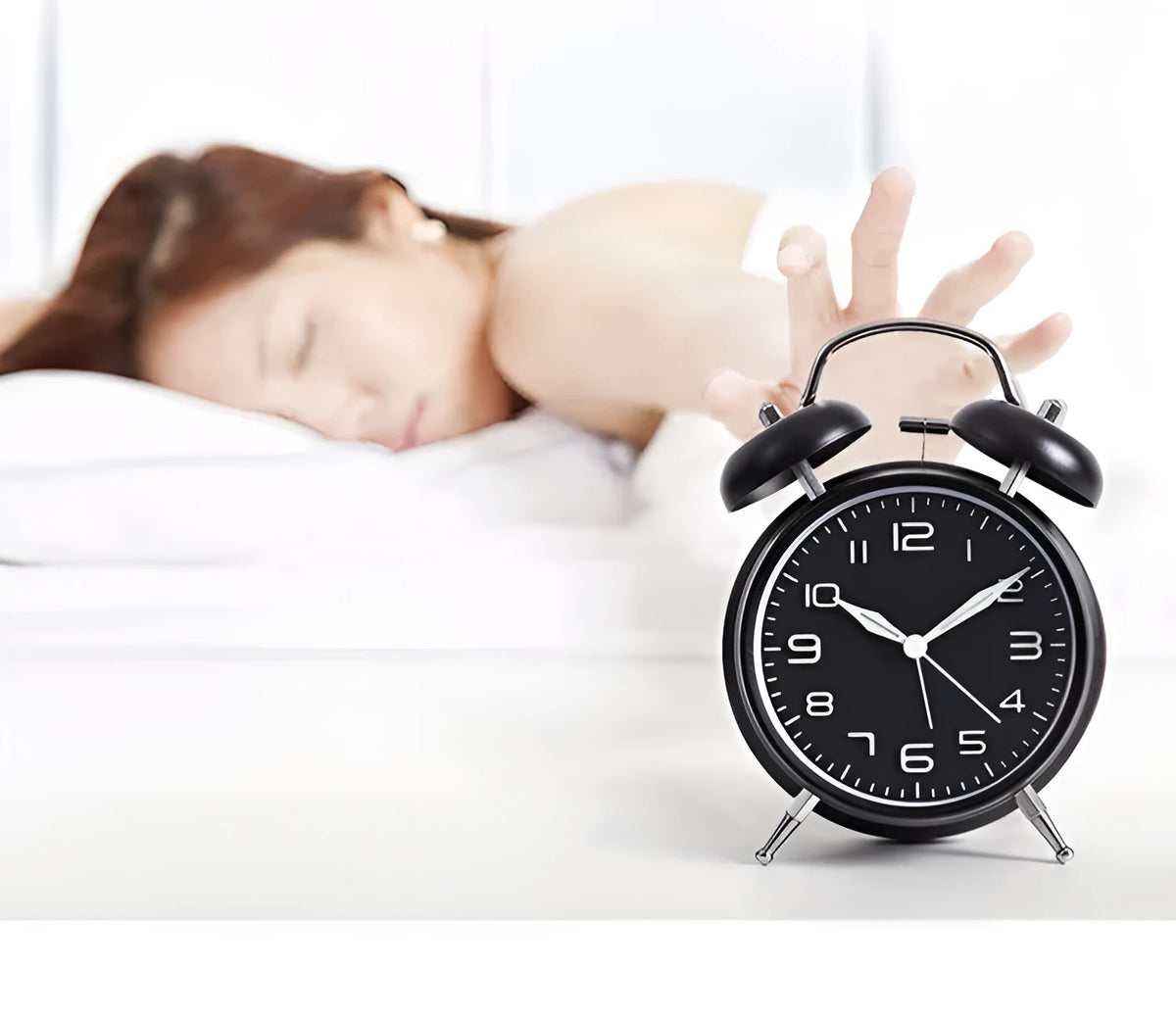 Large black metal alarm clock with luminous hands and face, 4 inches, on a wooden bedside table