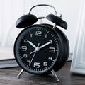 Large black metal alarm clock with luminous hands and face, 4 inches, on a wooden bedside table