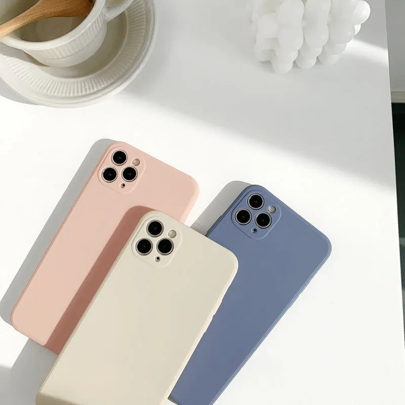 Simple solid colour silicone iPhone case in blue, pink, and white on a table