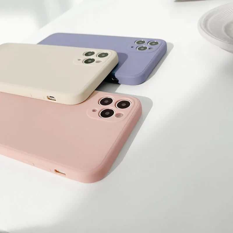 Simple solid colour silicone iPhone case in blue, pink, and white on a table