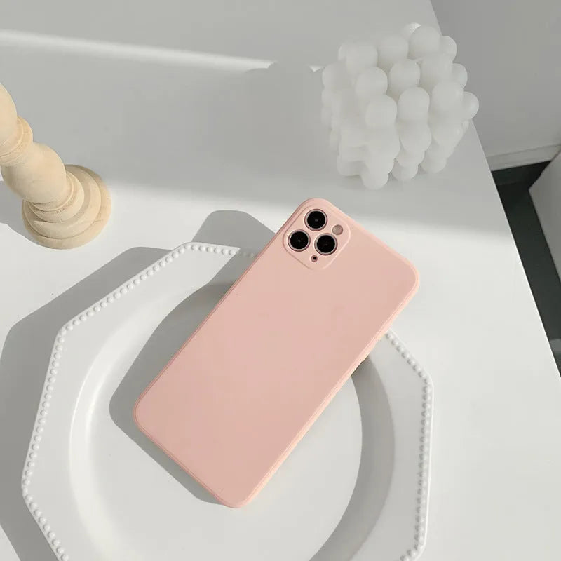 Simple solid colour silicone iPhone case in blue, pink, and white on a table