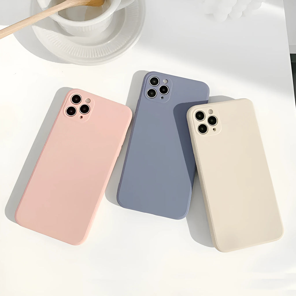 Simple solid colour silicone iPhone case in blue, pink, and white on a table