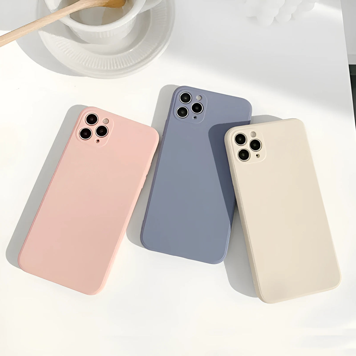 Simple solid colour silicone iPhone case in blue, pink, and white on a table